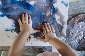 Cute little girl painting with her own hands, using tempera paint.