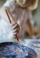 Close-up of child's hand holding paintbrush, painting with tempera paint.