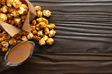 Obraz na płótnie Canvas Caramelized popcorn in paper bag on wooden kitchen table flat lay