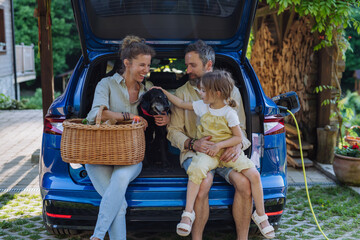Happy family sitting in a car trunk and waiting for charging.