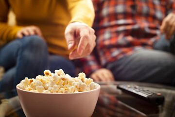 Caucasian couple sitting on sofa with popcorn and tv remote