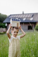 Portraitof little girl holding model of house with solar panels, concept of sustainable lifestyle...