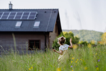 Rear view of little girl in front of family house with solar panels, concept of sustainable lifestyle and renewable resources.