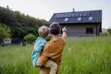 Rear view of father and his son looking at their house with solar panels on the roof.