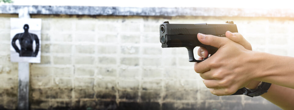 9mm pistol gun holding in hands of gun shooter aiming to the shooting target paper ahead at the shooting range, soft and selective focus, concept for recreational activity of humans.