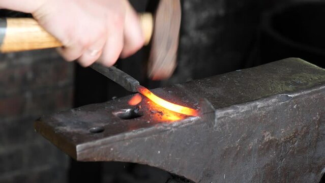 Blacksmith stokes a coal fire and pounds a red hot peice of metal with a hammer