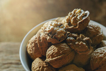 Raw brown organic walnut kernels with shell in a bowl on rustic wooden table. Selected focus