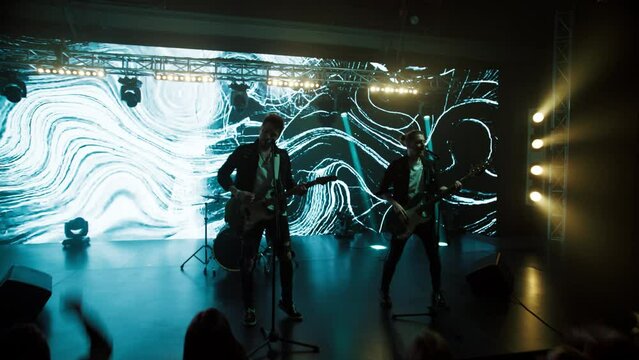 Jib shot of a rock band playing the gig during concert on stage of a large venue, surrounded by bright flashing stage lights