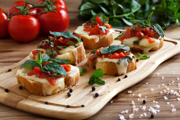 Bruschetta (sandwiches) with cherry tomatoes, mozzarella cheese and herbs on a cutting board on a dark background. 