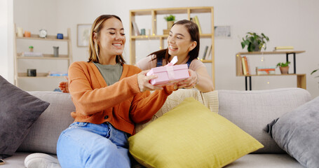 Home, lesbians and couple with a surprise, gift and bonding in living room, happiness and relax. Partners, women and queer people in their lounge, present and celebrate relationship, marriage and wow