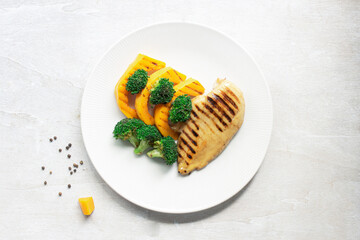 Healthy food grilled chicken has broccoli pumpkin vegetable in plate on white wood table.