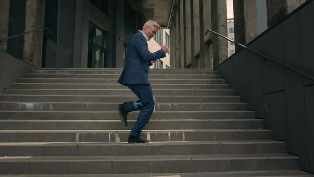 Happy Caucasian senior business worker employee mature man businessman dancing walking on stairs near office building outside outdoors funny moving dance success celebrate victory achieve having fun