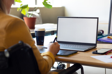 Caucasian casual businesswoman in wheelchair using graphics tablet and laptop, copy space on screen