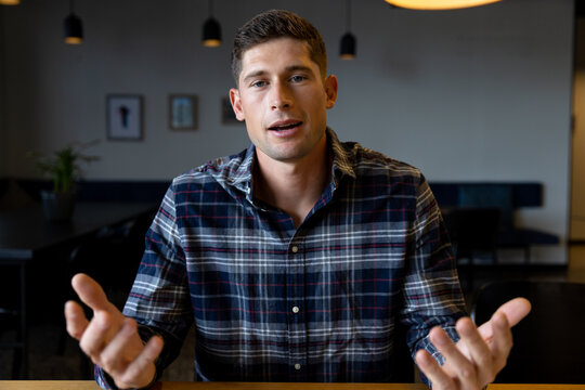 Happy caucasian casual businessman talking and gesturing during video call at desk in office