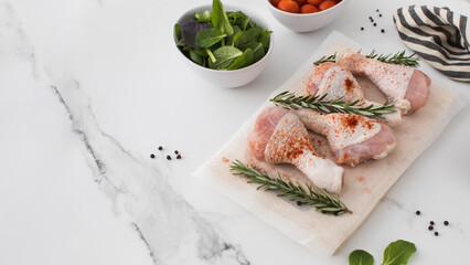 Raw chicken legs with spices and rosemary sprigs on a wooden cutting board. Copy space