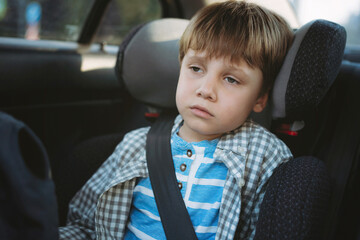 Little boy feeling sick travelling by car sitting in child seat fastened with belt