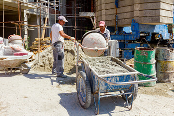 Wheelbarrow with mortar and empty cement mixer machine placed on construction site - obrazy, fototapety, plakaty