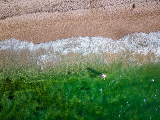 Woman bathing and swimming on the coast of the Peloponnese in green, crystal clear water on a romantic beach with rocks and forest in the background