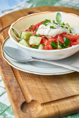 Fresh summer salad with tomatoes, cucumbers, onions and sour cream in light colors on a wooden kitchen cutting board.