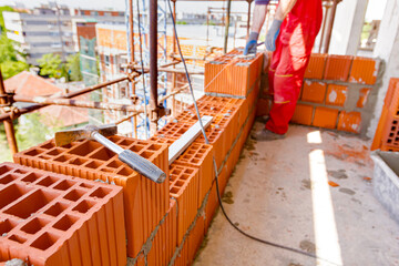 Metal handled hammer on red ceramic block, building a wall of unfinished building
