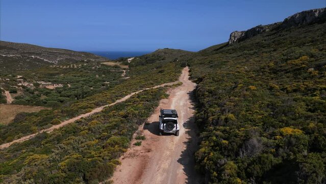 White 4x4 offroad vehicle driving a reddish offroad trail through the wilderness towards the coast