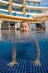 Little girl playing in outdoor swimming pool, jumping into water on summer vacation . Child learning to swim in outdoor pool of luxury resort.