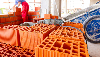 Electric drill tool on pile of red blocks, worker builds wall with bricks and mortar, building site