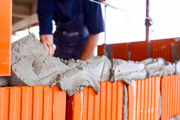 Builder using spatula to set up mortar over red brick, building site