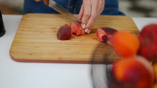 High angle view female Caucasian hands cutting flat peach on wooden board. Close-up unrecognizable young woman slicing delicious fruit in kitchen at home