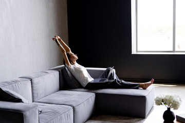 Business woman wearing white shirt sitting on sofa with laptop raising her arms above her head stretching