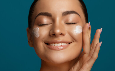 Close up beauty portrait of a beautiful young woman applying face cream, female model with closed...