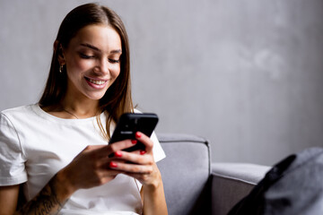 Happy woman relaxing on comfortable sofa using smartphone chatting in social networks, watching funny videos at home.