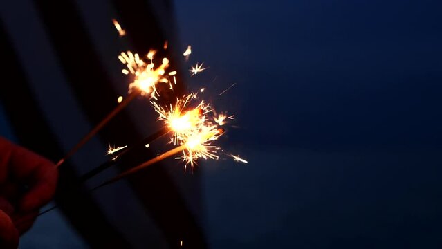 Hand holding sparklers fireworks celebration fourth of July, USA Independence Day July 4th on America flag background. Concept 4th of July, Holiday, USA, Freedom, Juneteenth, Memorial, Veterans, Day