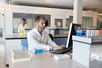 Male scientist studying data on a computer in a busy laboratory