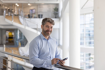 Hispanic businessman holding a smartphone in modern corporate office atrium
