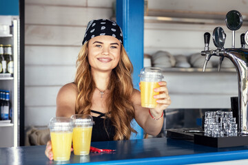 Hipster girl bartender serving fresh lemonade behind counter at outdoor bar during summer festival - 615104828