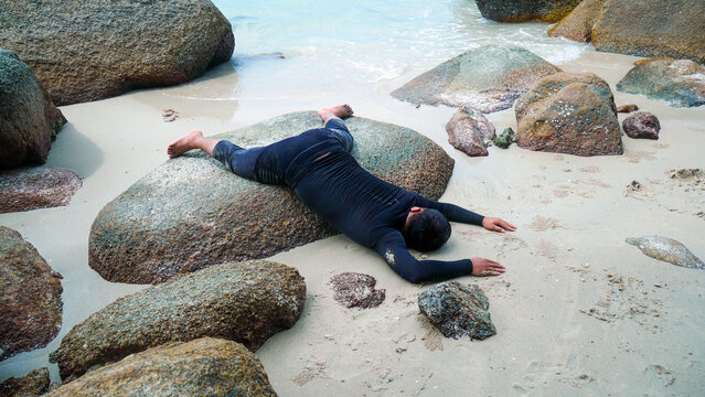 Cute sleeping teenage boy on beach rocks in pants and a swimsuit. Cute sleeping styles on vacation. Summertime concept. Copy space.