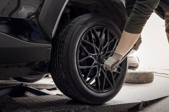 A master tire fitter screws a new black wheel to a car in a tire service, close-up
