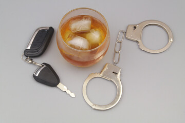 Glass with alcohol, steel handcuffs and car key on gray background. Drunk driving concept.