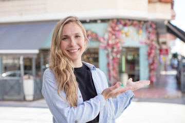 pretty woman feeling happy and cheerful, smiling and welcoming you, inviting you in with a friendly gesture