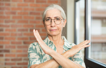 senior pretty woman looking annoyed and sick of your attitude, saying enough! hands crossed up...