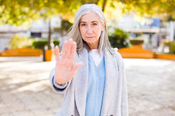 senior retired pretty white hair woman looking serious, stern, displeased and angry showing open...