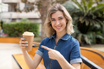 pretty woman smiling cheerfully, feeling happy and pointing to the side. take away coffee concept - obrazy, fototapety, plakaty
