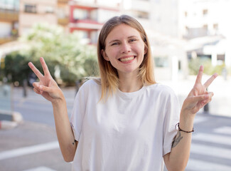 pretty young woman smiling and looking happy, friendly and satisfied, gesturing victory or peace with both hands