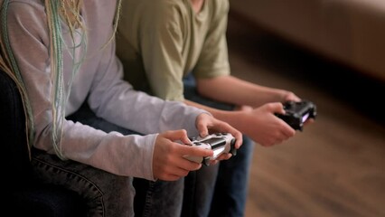 kids hands with joysticks, two children siblings playing video game console while sitting at home, real people, leisure concept.
