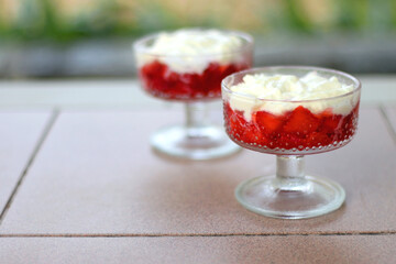 Two bowls of strawberries and whipped cream, served in a garden. Selective focus.