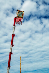 Pole decorated in white and red with a picture of a saint at the top. Cloudy and dark blue sky. Vertical.