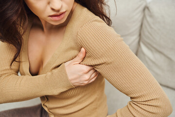 Cropped view of young brunette woman in brown jumper touching lymphatic nodes on armpit for...