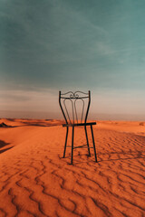 Naklejka premium Chair in desert: An intriguing sight, a lone chair stands amidst the barren expanse, a silent enigma that sparks curiosity and imagination.