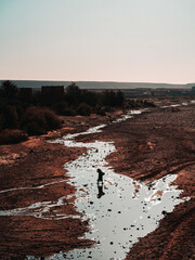 River crossing: A woman strides across a dry riverbed, embodying resilience and unwavering determination amidst challenging terrain.